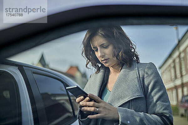Frau benutzt Mobiltelefon an offener Autotür