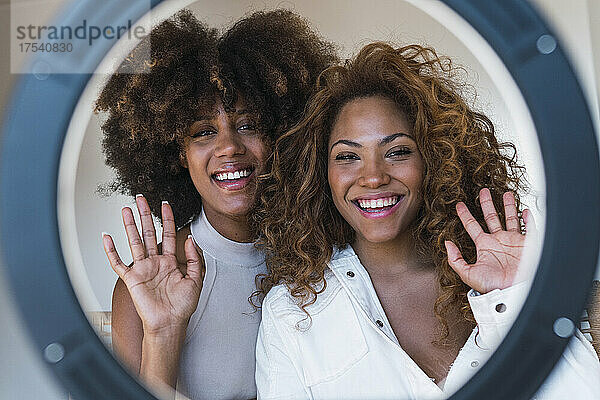 Smiling friends waving hands through ring light at home