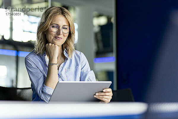 Smiling businesswoman with hand on chin using tablet PC in office