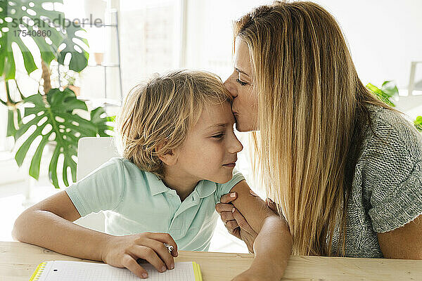 Mother kissing son on forehead at home