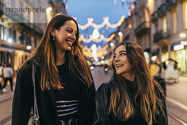 Young friends smiling at each other walking in city