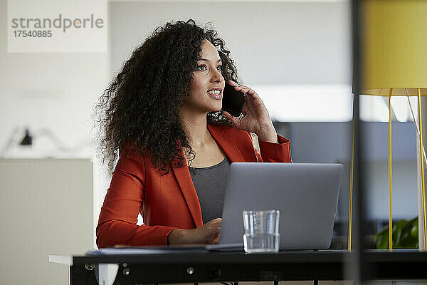 Geschäftsfrau mit Laptop spricht im Büro auf Smartphone