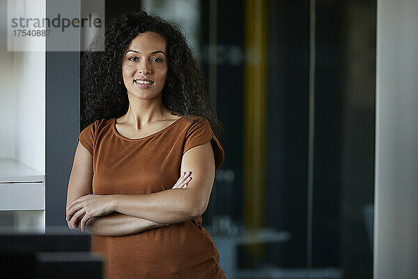 Smiling businesswoman leaning with arms crossed at workplace