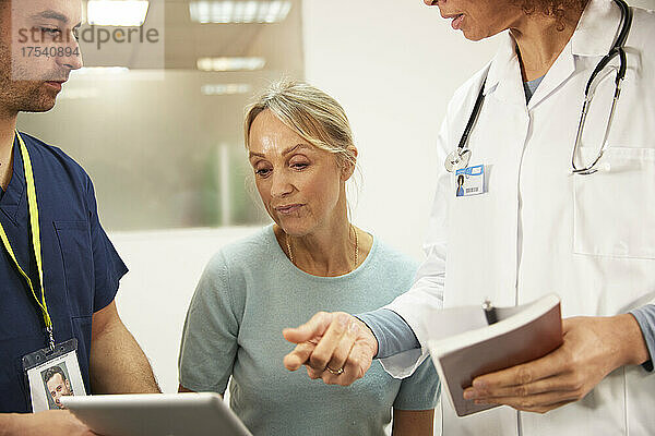 Älterer Patient schaut von Mitarbeitern des Gesundheitswesens im Krankenzimmer auf den Tablet-PC