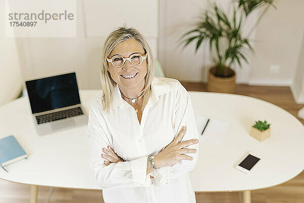 Happy businesswoman with arms crossed at workplace