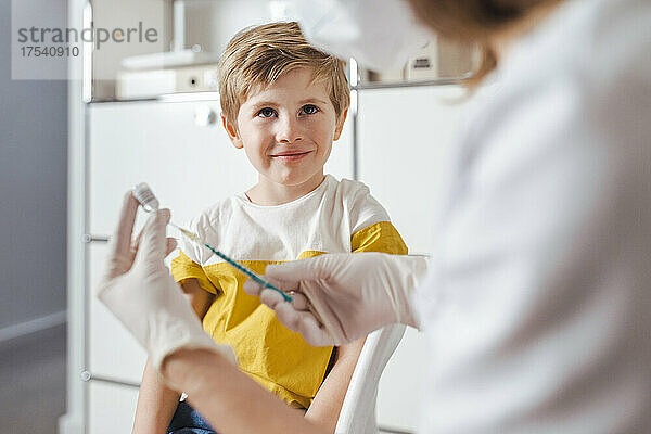 Lächelnder Junge blickt in der Mitte auf den Arzt  der die Impfinjektion vorbereitet