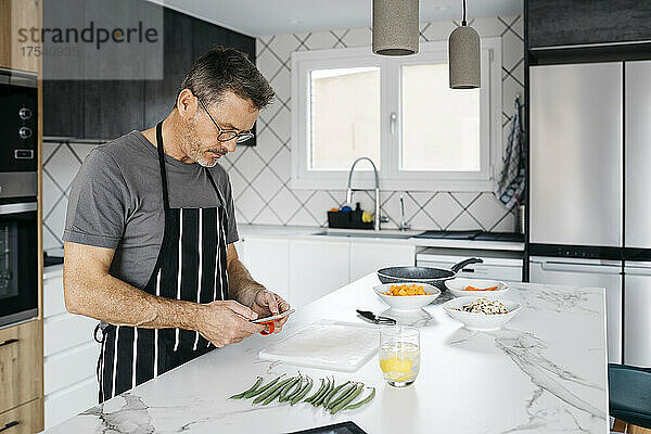 Mann benutzt Smartphone auf Kücheninsel