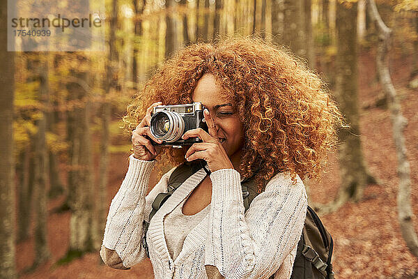 Woman with brown curly hair photographing in autumn forest