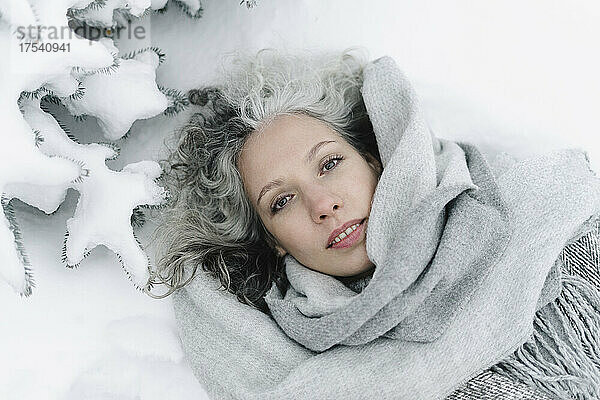 Woman with gray scarf lying on snow covered landscape