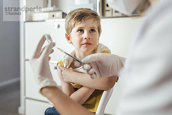 Junge blickt in der Mitte auf den Arzt  der die Injektion des COVID-19-Impfstoffs vorbereitet