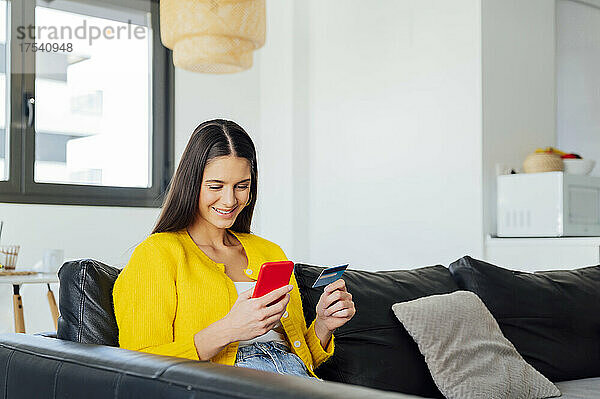Smiling woman doing online shopping on smart phone in living room