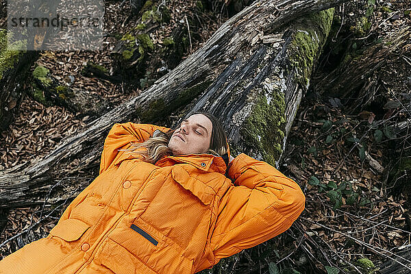 Hiker relaxing on fallen moss covered tree in forest