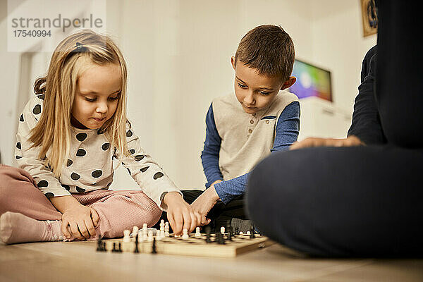 Brother and sister playing chess with grandfather at home