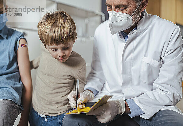 Arzt füllt Impfpass mit Jungen in der Mitte aus