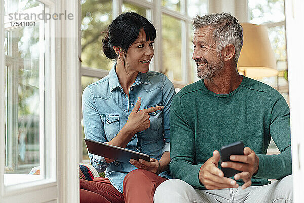 Woman holding tablet PC talking with smiling man at home