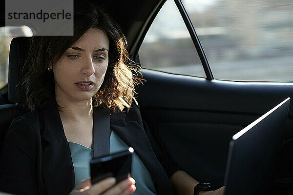 Geschäftsfrau mit Laptop nutzt Mobiltelefon im fahrerlosen Auto