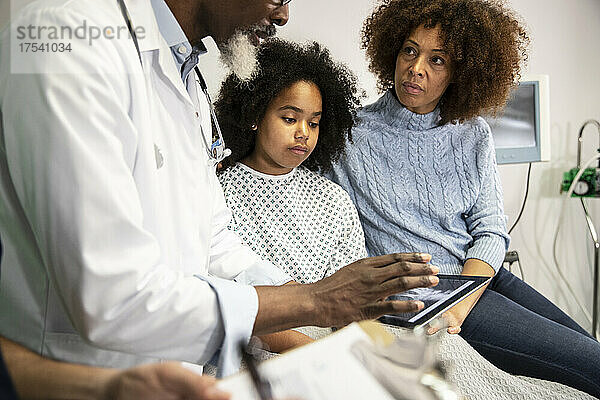 Frau und kranke Tochter schauen sich Arzt an  der Bericht auf Tablet-PC im Krankenhaus teilt