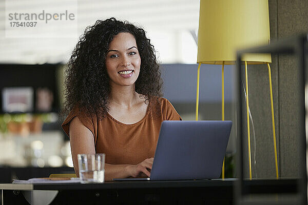 Smiling businesswoman with laptop on desk at workplace
