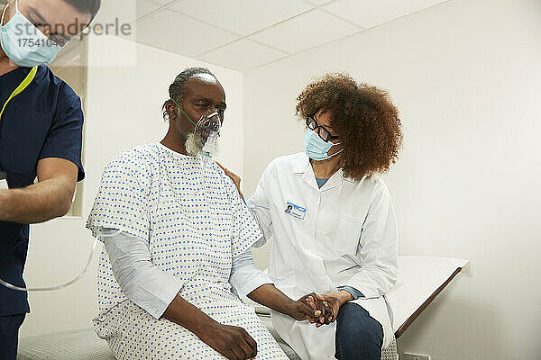 Ärztin tröstet Patientin mit Sauerstoffmaske im Krankenzimmer