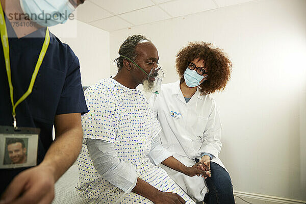 Arzt sitzt mit Patient mit Sauerstoffmaske im Krankenzimmer