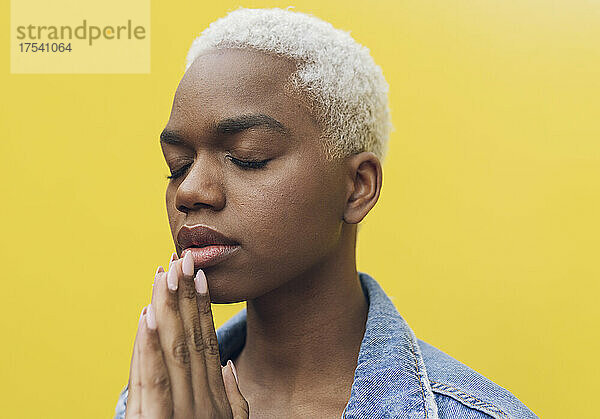 Woman with hands clasped meditating against yellow background