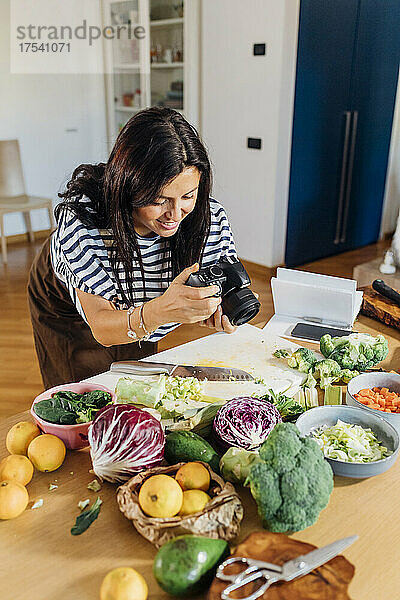 Frau fotografiert frisches Gemüse mit Digitalkamera zu Hause