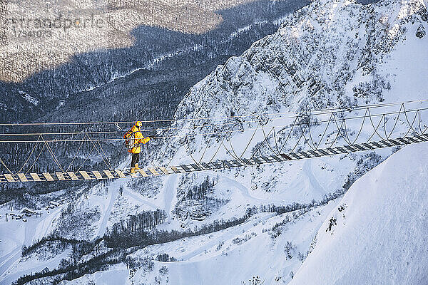 Mann wandert auf Hängebrücke über schneebedeckten Berg