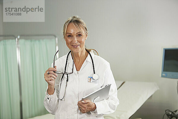 Lächelnder Arzt mit Brille und Tablet-PC im Krankenzimmer