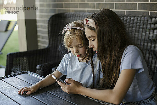 Girl sharing smart phone with sister at patio