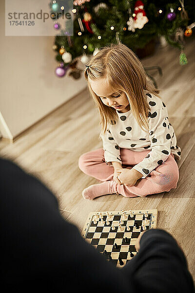 Cute girl playing chess with grandfather at home