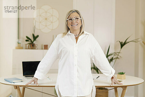 Lächelnde Geschäftsfrau  die am Arbeitsplatz vor dem Schreibtisch steht