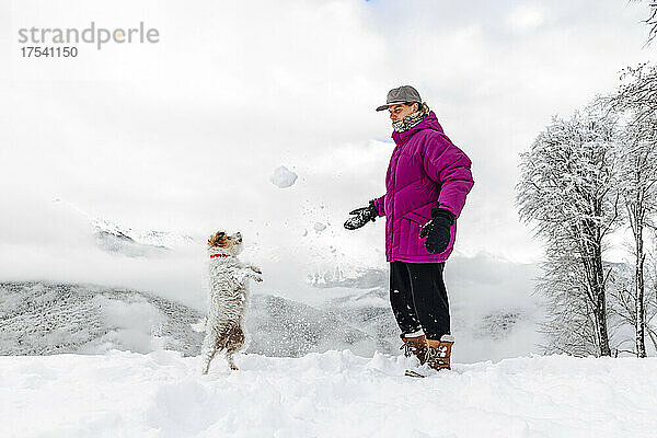 Mann und Hund spielen mit Schnee