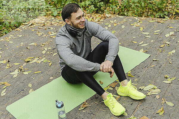 Smiling man resting on exercise mat at park