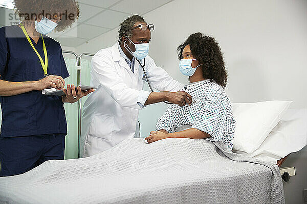 Arzt steht der Krankenschwester zur Seite und untersucht den Patienten während einer Pandemie im Krankenhaus