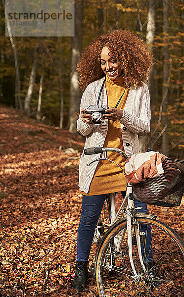 Smiling woman looking at camera on bicycle in autumn forest