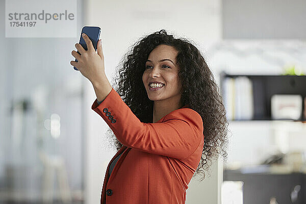 Lächelnde Geschäftsfrau  die am Arbeitsplatz ein Selfie mit dem Smartphone macht