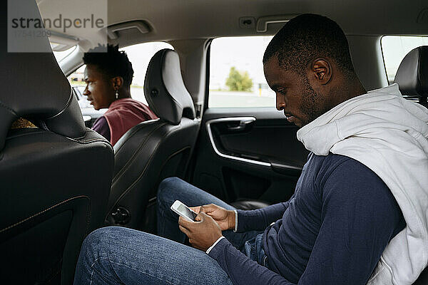 Junger Mann nutzt Smartphone mit Freunden im Auto auf Roadtrip