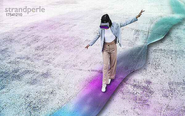 Teenage girl using virtual reality simulator with arms outstretched walking on multi colored wave path