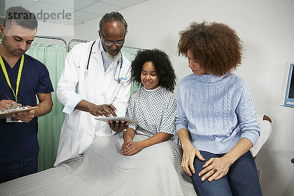Patientin und Mutter überprüfen Bericht über Tablet-PC  der vom Arzt im Krankenhaus gehalten wird
