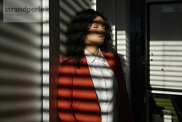 Geschäftsfrau steht mit geschlossenen Augen im Sonnenlicht am Arbeitsplatz