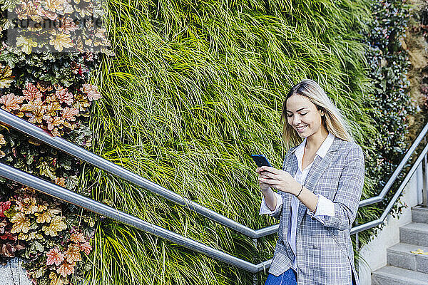 Smiling businesswoman using smart phone by plants