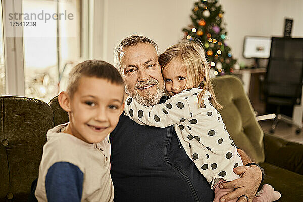Mädchen umarmt Großvater und sitzt mit Enkel zu Hause auf dem Sofa
