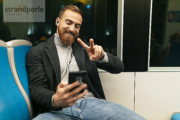 Man taking selfie through smart phone with peace sign in tram