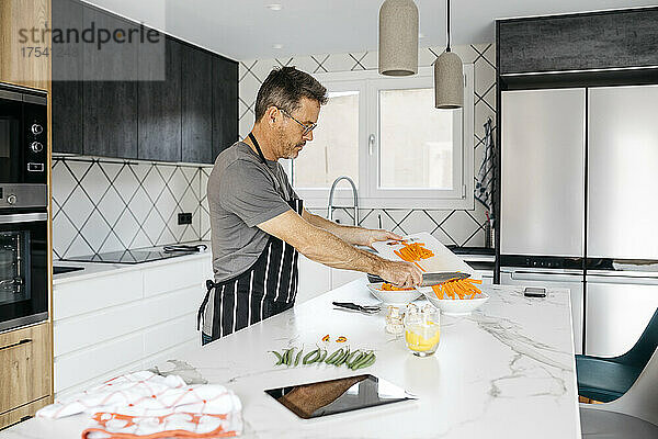 Mann legt gehackte Karotten in eine Schüssel und bereitet zu Hause Essen zu