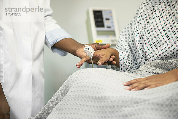 Doctor examining pulse of patient with oximeter at hospital