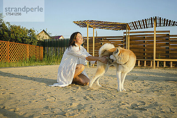 Lächelnde Frau spielt mit Akita-Hund auf Sand