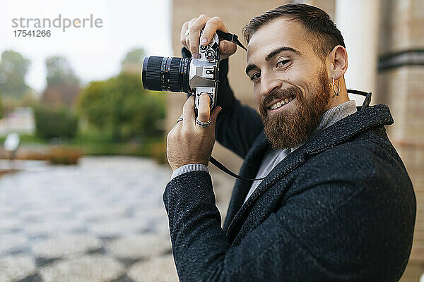 Lächelnder junger bärtiger Mann mit Kamera
