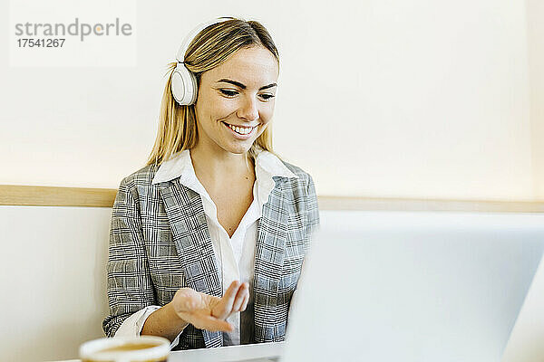 Lächelnder blonder Freiberufler mit Kopfhörern bei Videoanruf über Laptop im Café