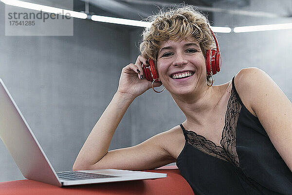 Cheerful businesswoman with laptop and wireless headphones