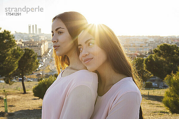 Smiling woman embracing thoughtful sister at sunset